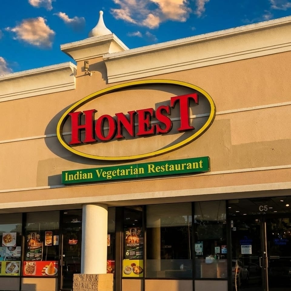 Exterior of Honest Indian Vegetarian Restaurant with a large red and yellow sign under a blue sky.