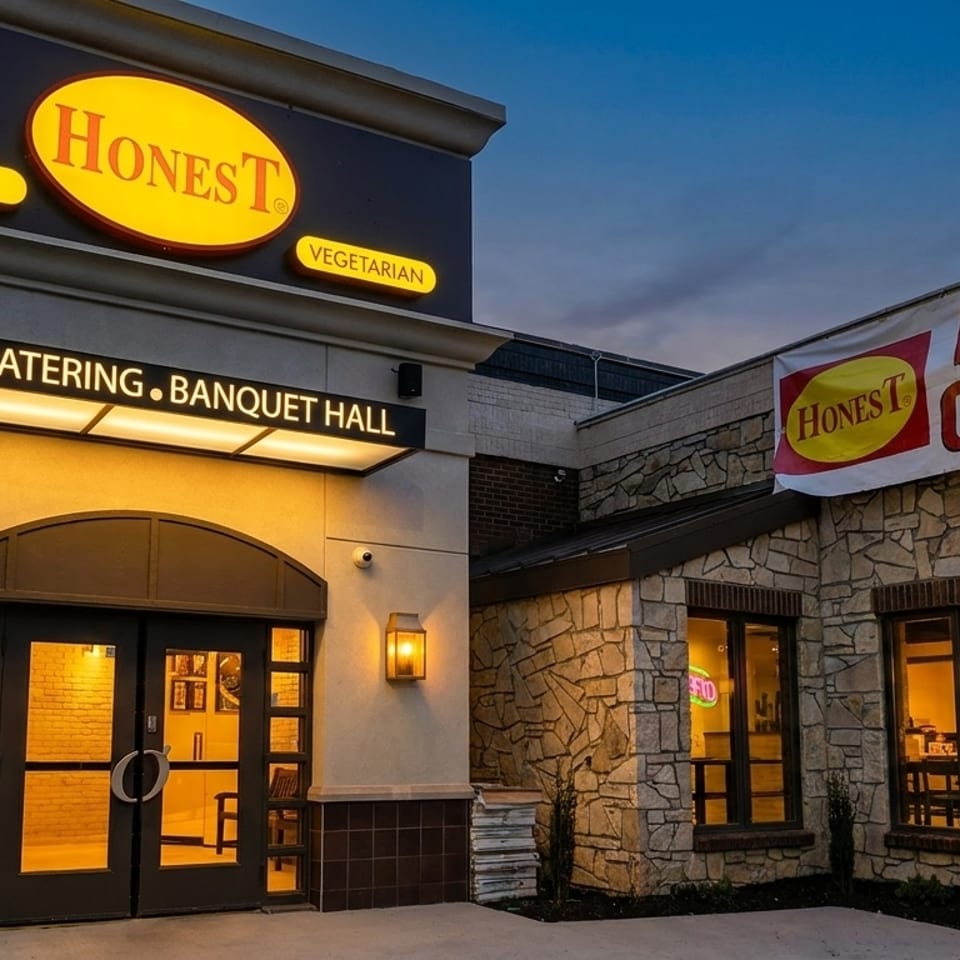 Exterior of Honest restaurant at dusk, with "Now Open" banner and illuminated signs for Indian Vegetarian cuisine.