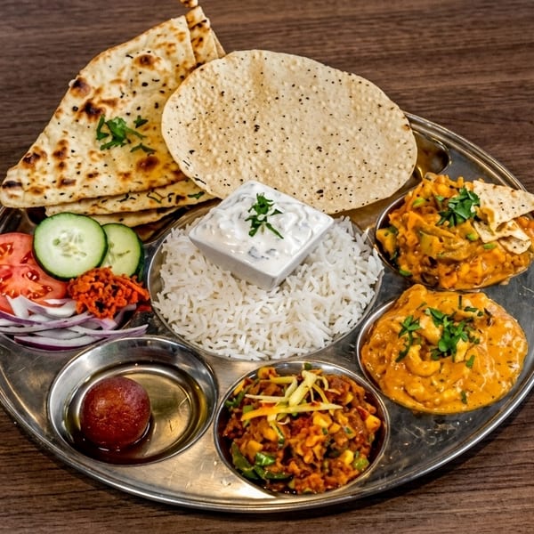 A traditional Indian thali with various dishes, including naan, rice, curries, and dessert.